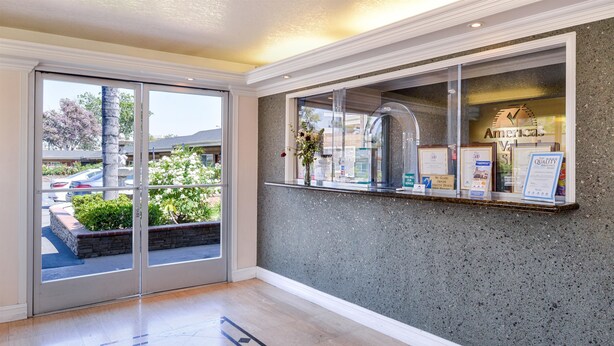 A reception area with a glass door leading outside, a counter with awards, and a view of parked cars and greenery.
