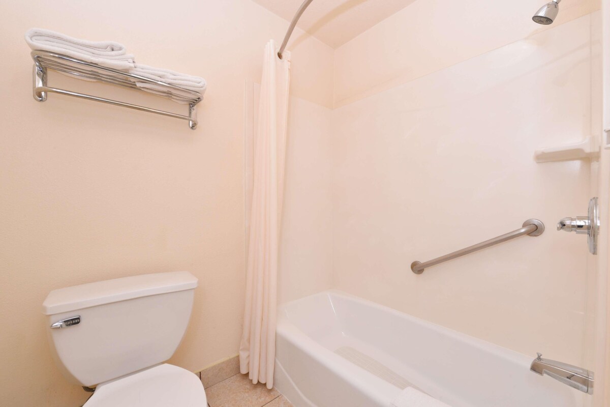Un baño con inodoro, ducha con barra de apoyo y toallero.