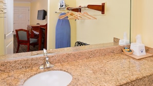 A hotel bathroom with a granite countertop sink, a mirror, a towel rack, and a hanging blue towel.