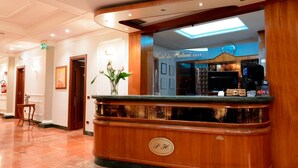 Een hotel receptie met een houten receptiebalie, een klok en een bord met de tekst 'Hotel dei Platani'.