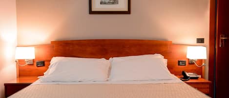 Habitación de hotel con cama doble, dos lámparas de noche, un cuadro en la pared y cabecera de madera.