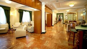 Een hotel lobby met een marmeren vloer, leren banken en een eetgedeelte met tafels en stoelen.
