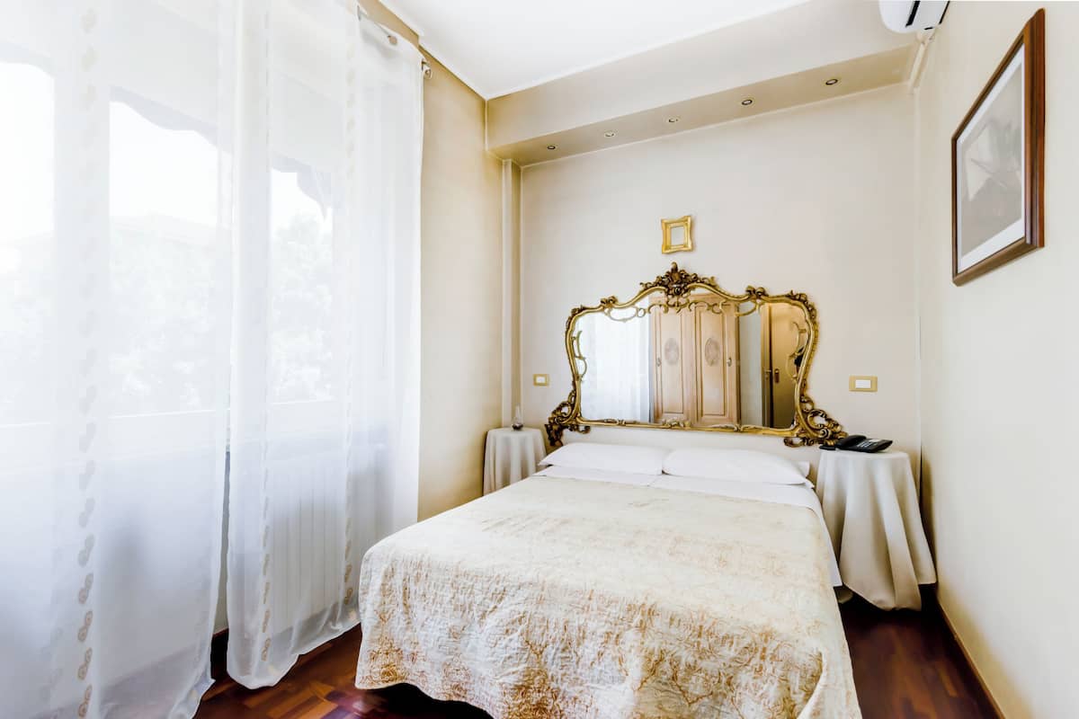 A hotel room with a large bed, a classic ornate mirror, and a small table with a phone.