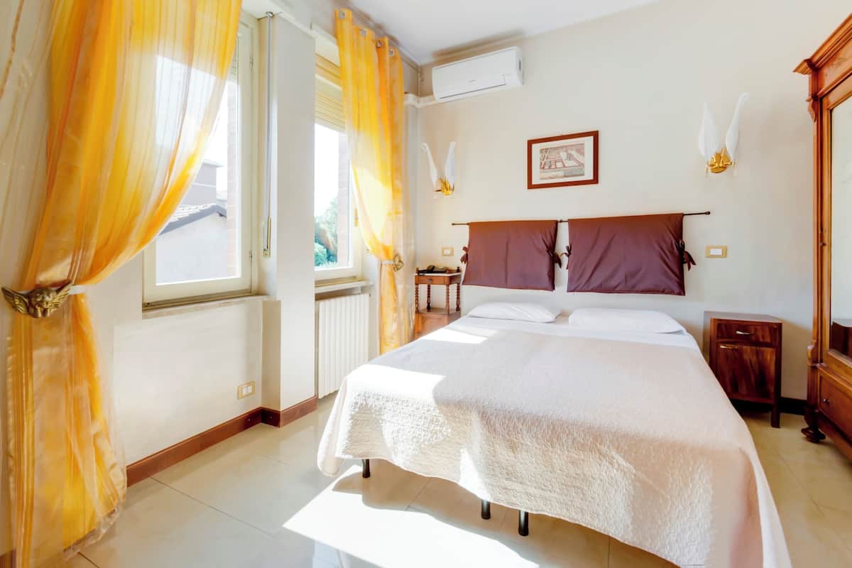 A neatly arranged bedroom with a large bed, a bedside table, a nightstand, and a window with curtains.