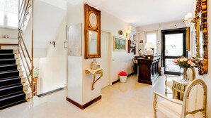 A spacious hallway with a staircase, a console table with a vase of flowers, and a dining area with a table and chairs. - Hotel Original (Turin)