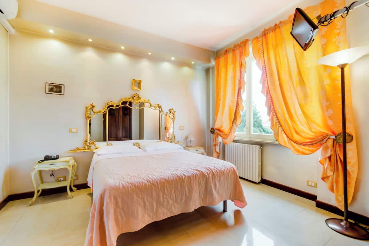 A bedroom with a large bed, a vanity with a mirror, a bedside table, and a window with curtains.