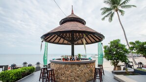 A beachside bar with a stone structure, wooden stools, and a view of the ocean. - Samaya Wellness Resort (Koh Samui)
