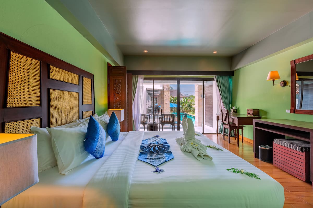 A hotel room with a large bed, a desk, and a view of the outdoor area.