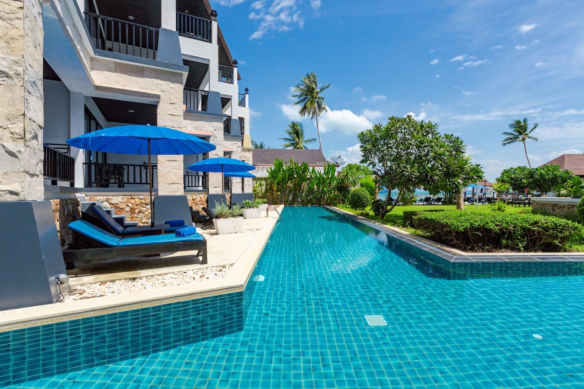 A swimming pool with blue tiles, lounge chairs, and umbrellas.
