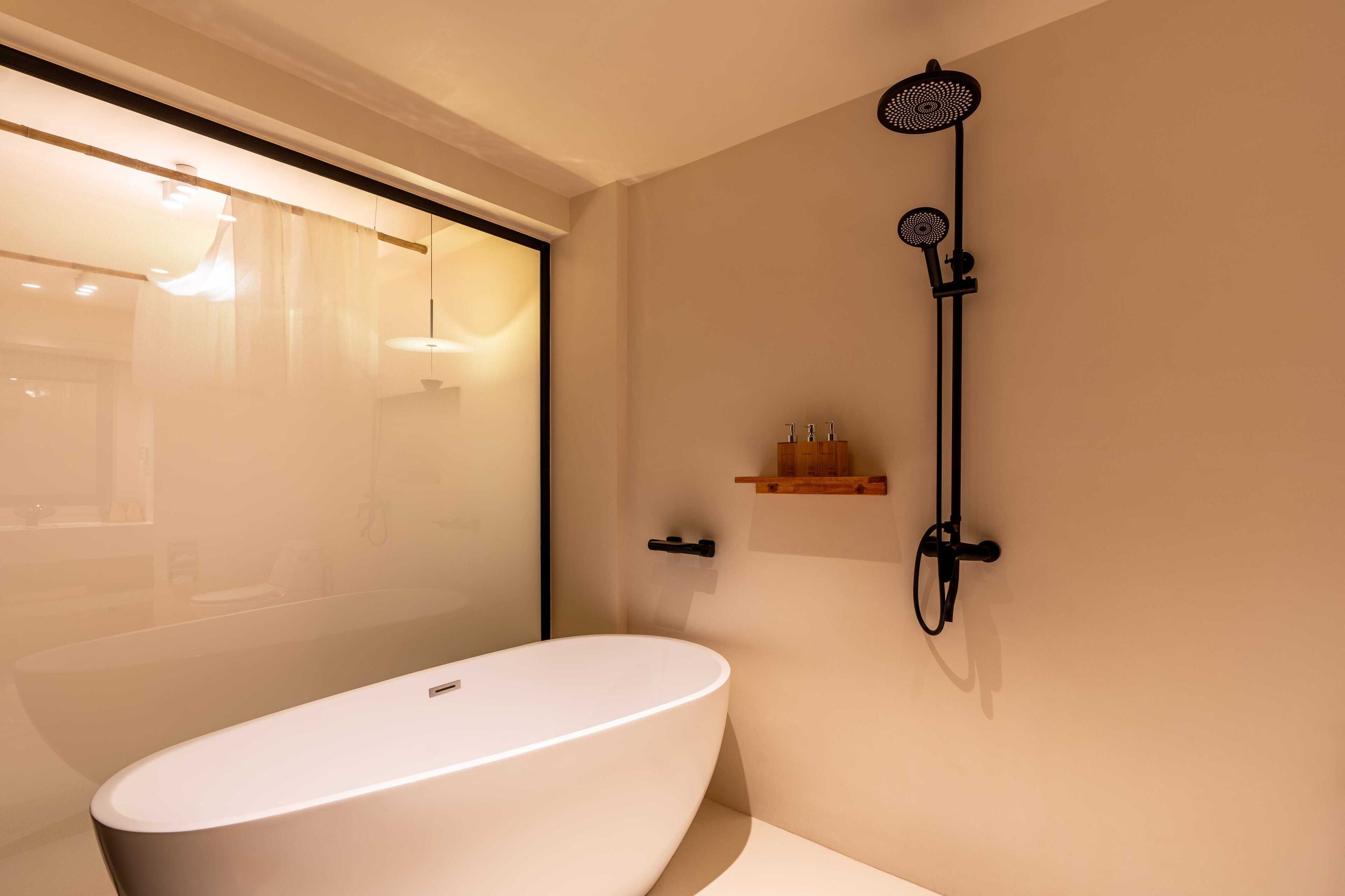 Une salle de bain moderne avec une baignoire sur pieds, une pomme de douche fixée au mur et une petite étagère en bois où sont rangés les articles de toilette.