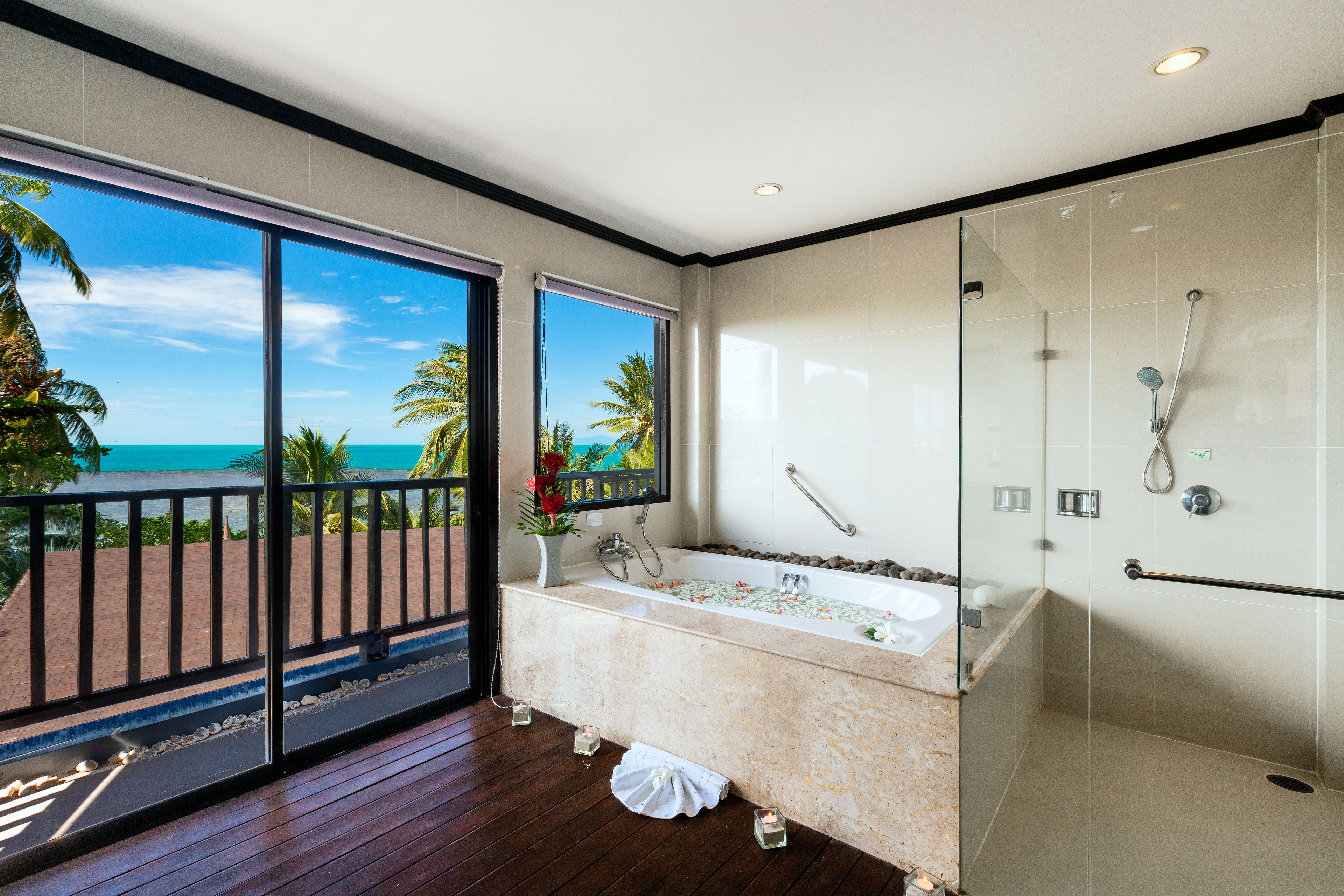 A modern bathroom with a large bathtub, a glass shower enclosure, and a view of the ocean through large windows.