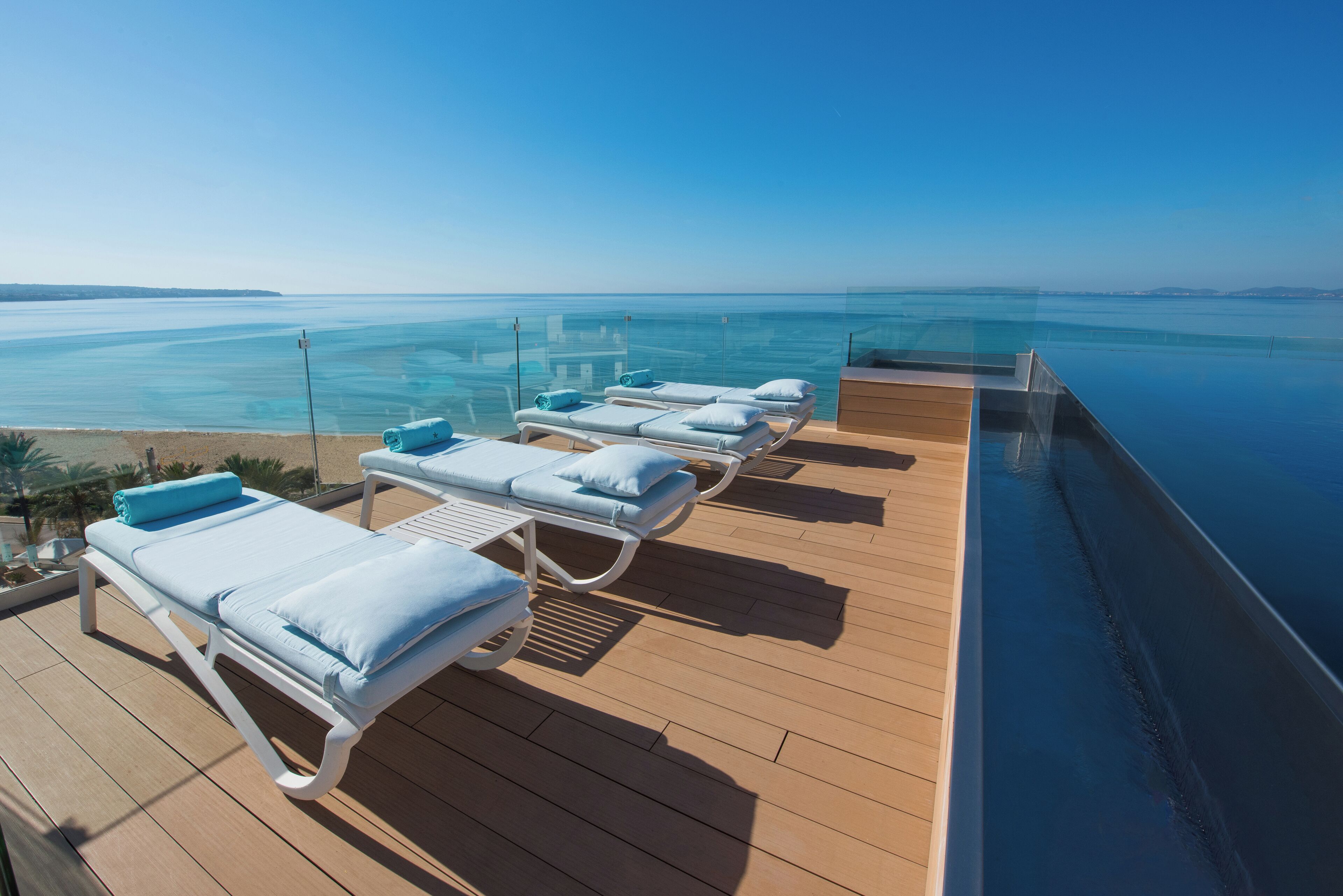 A sun deck with lounge chairs and an infinity pool overlooking the sea.