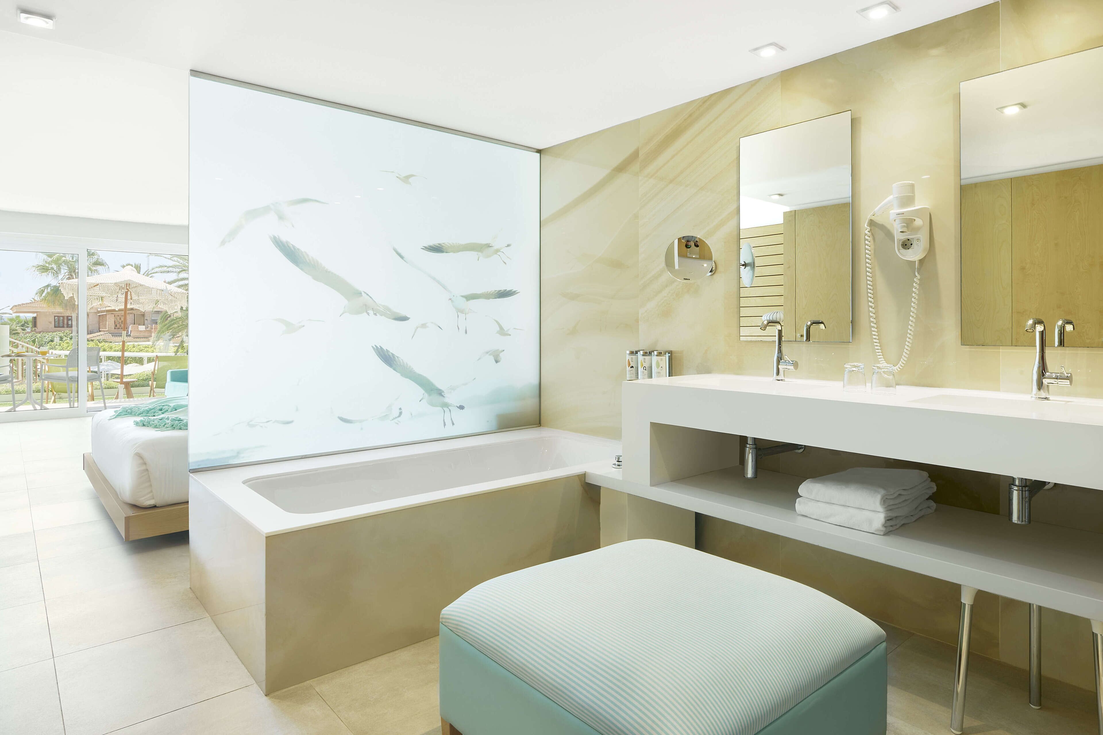 A modern bathroom with a large bathtub, a vanity with a mirror, and a bench.