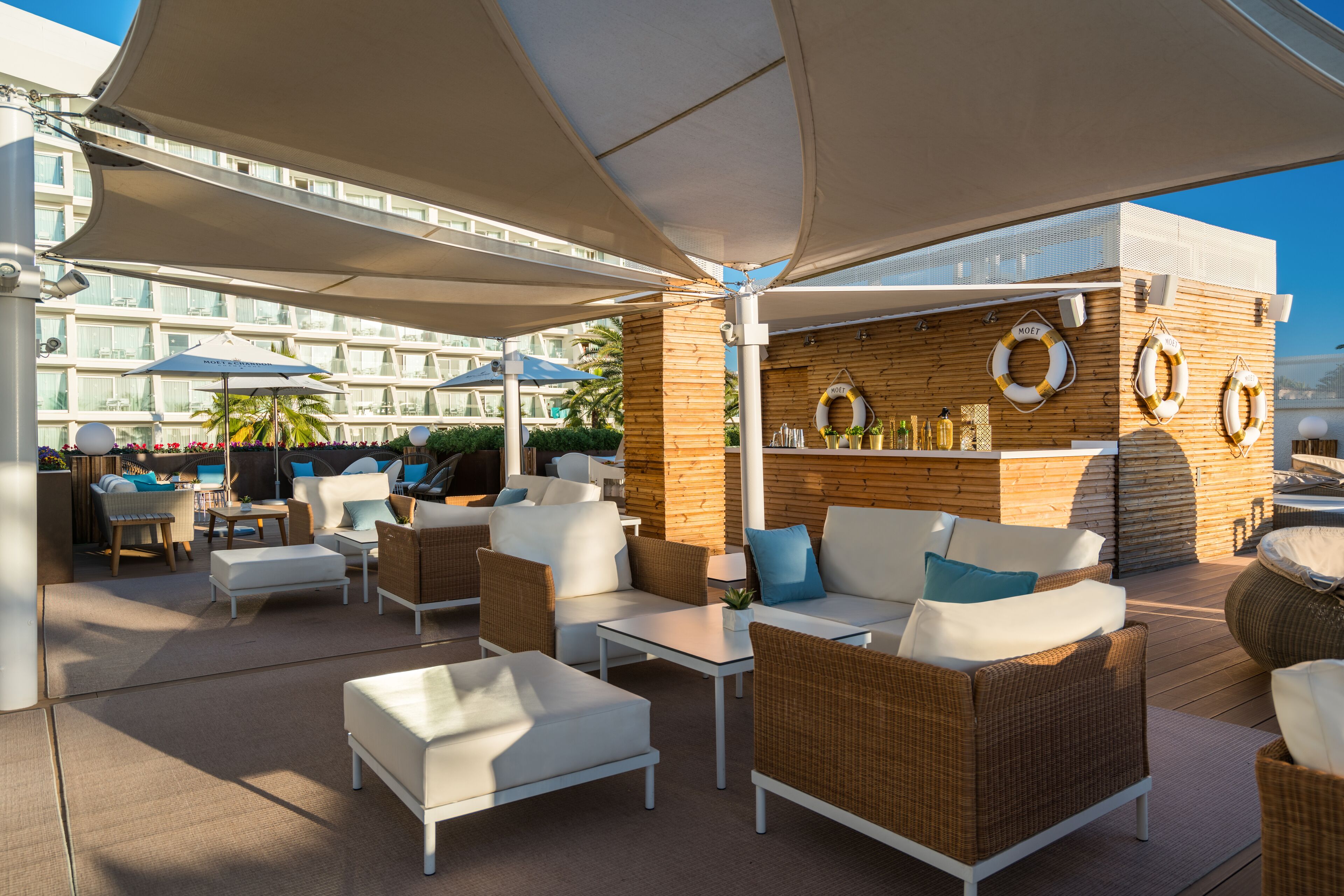 An outdoor lounge area with wicker furniture, umbrellas, and a wooden wall with life rings.
