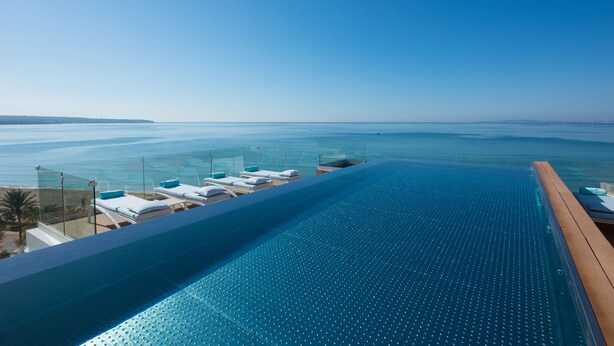 Una piscina infinita con vista despejada al océano y a la playa.