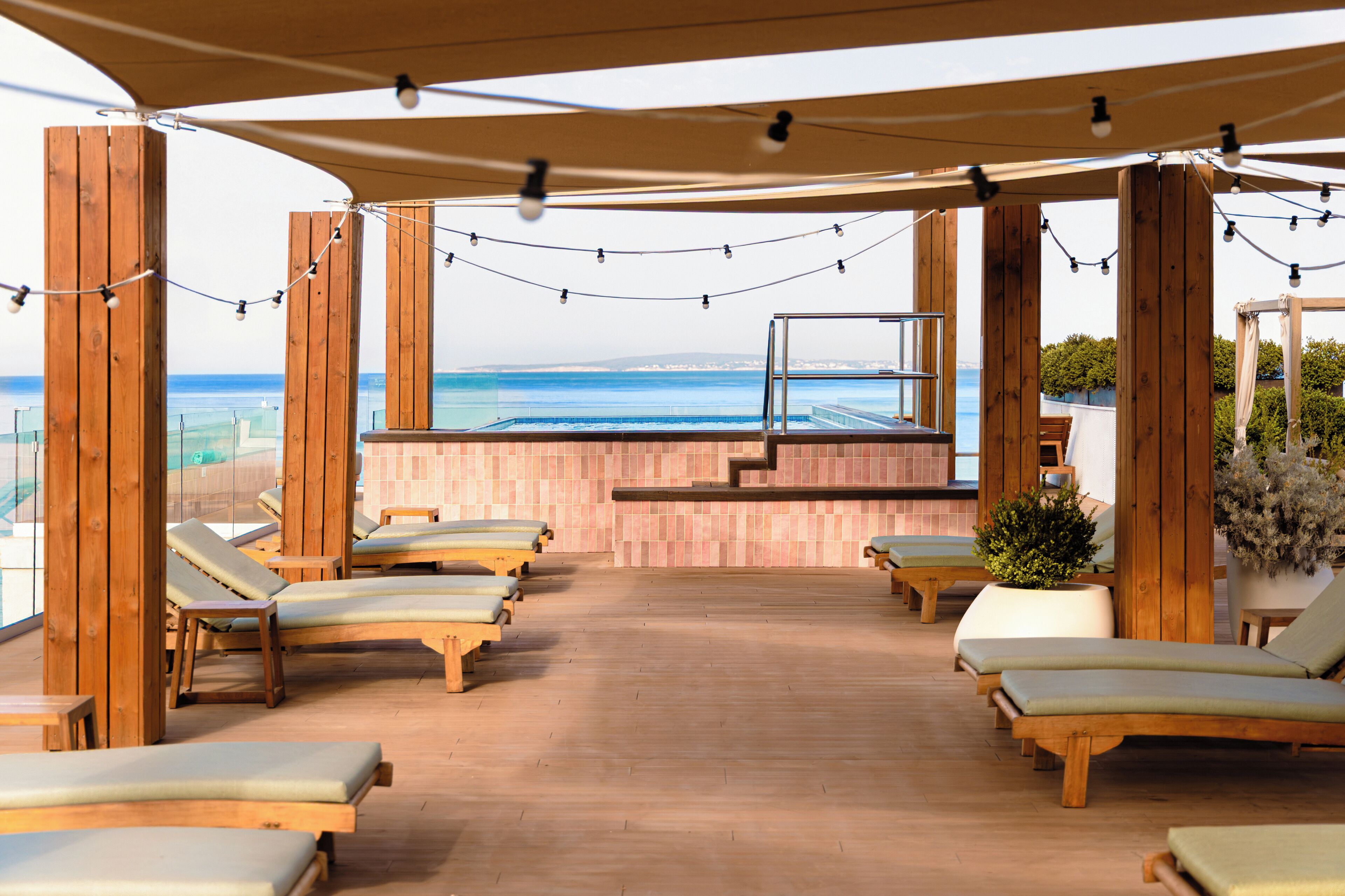 A sunlit outdoor lounge area with wooden furniture and a view of the sea.