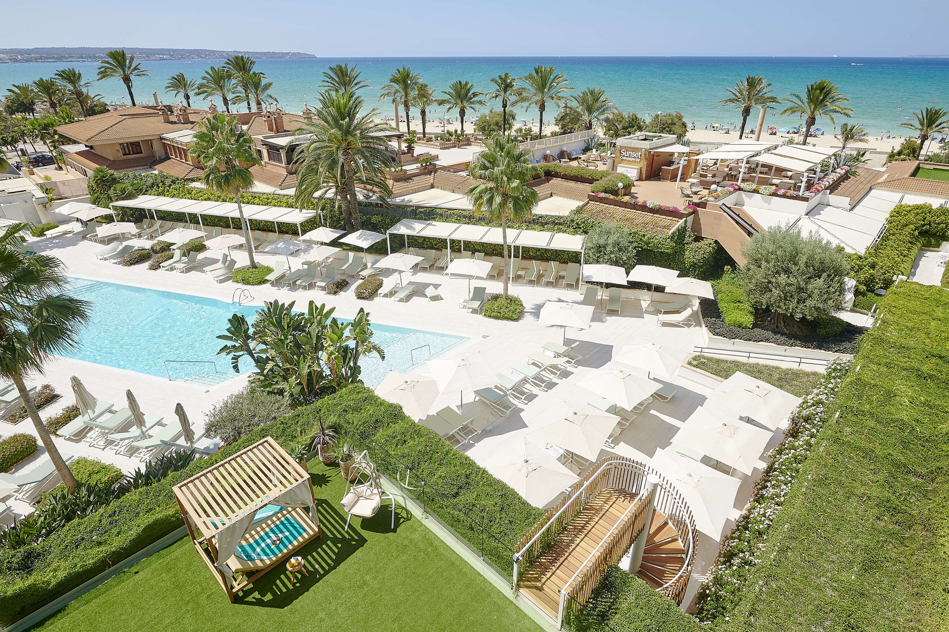 A resort with a pool, sun loungers, and palm trees.