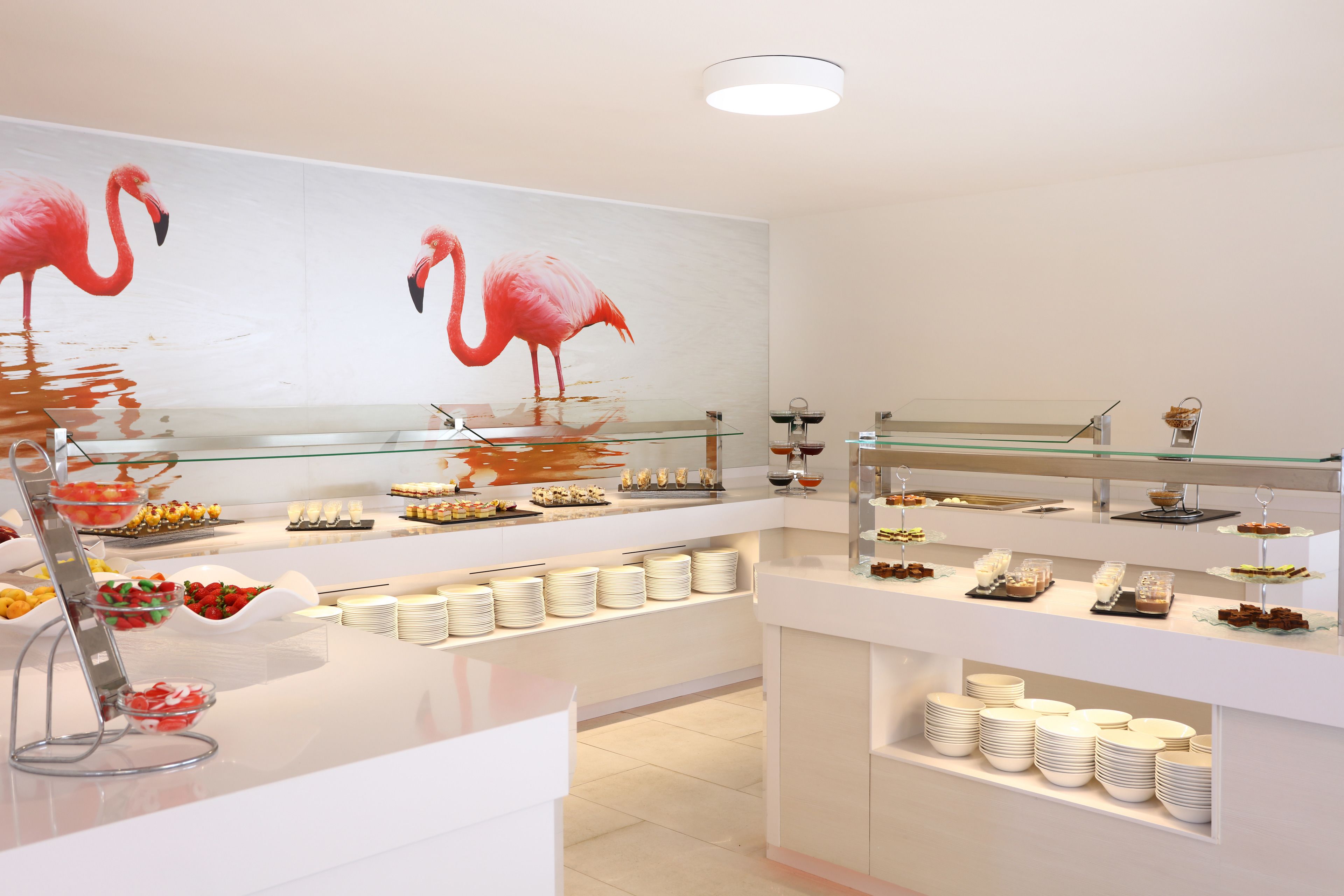 Ein Buffetbereich mit verschiedenen Servierstationen, Glasvitrinen und einer Wandmalerei von Flamingos.