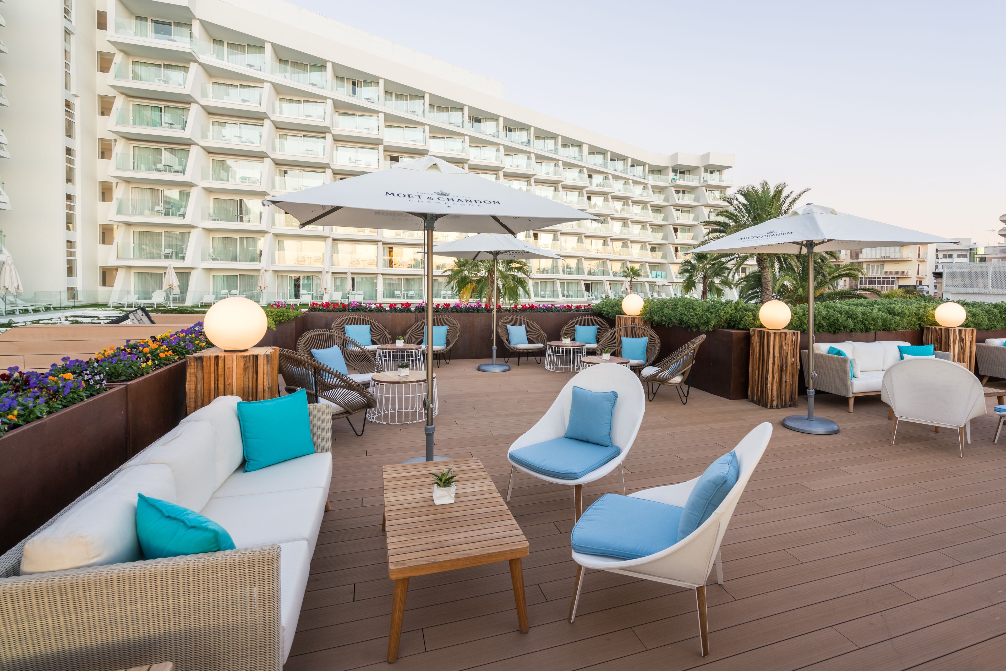 A rooftop lounge area with outdoor seating, umbrellas, and a view of a hotel building.