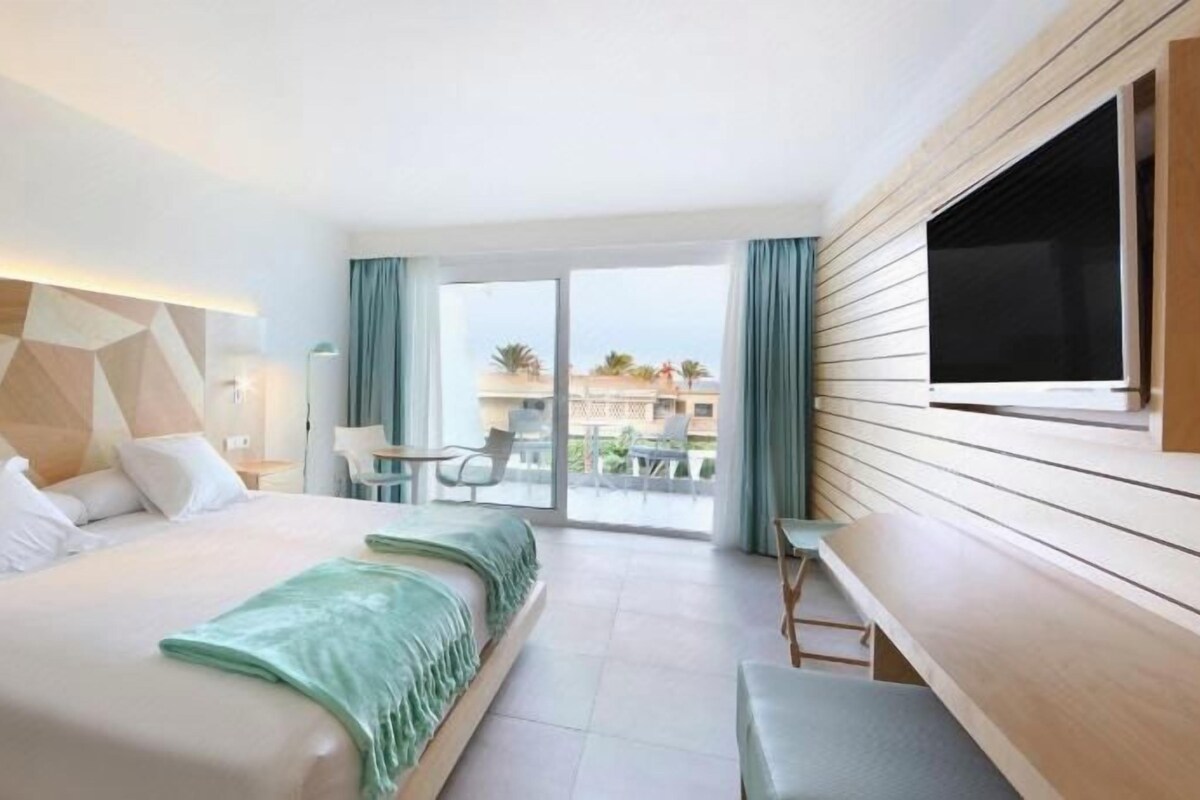 A hotel room with a bed, a TV, a desk, and a balcony with a view.