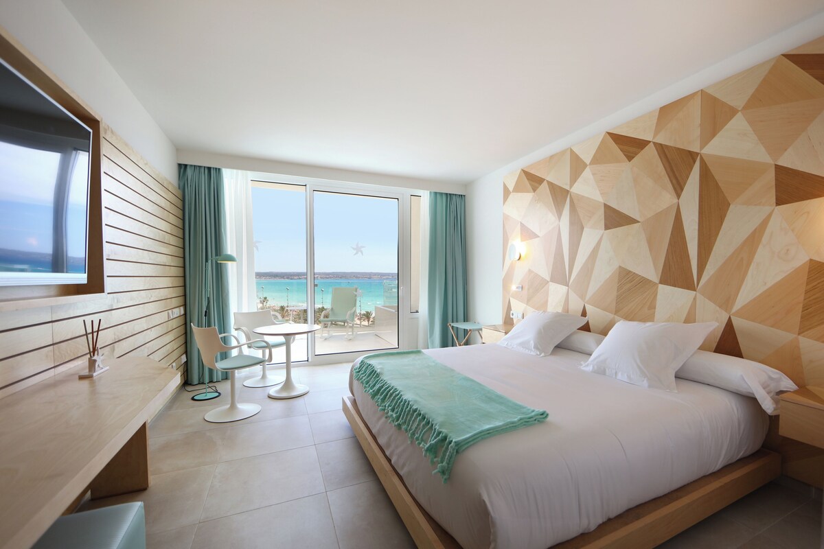 Habitación de hotel con cama, escritorio, silla, mesita y vista al mar.