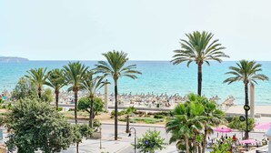 Un paseo marítimo frente a la playa, con palmeras, sombrillas y vistas al mar.