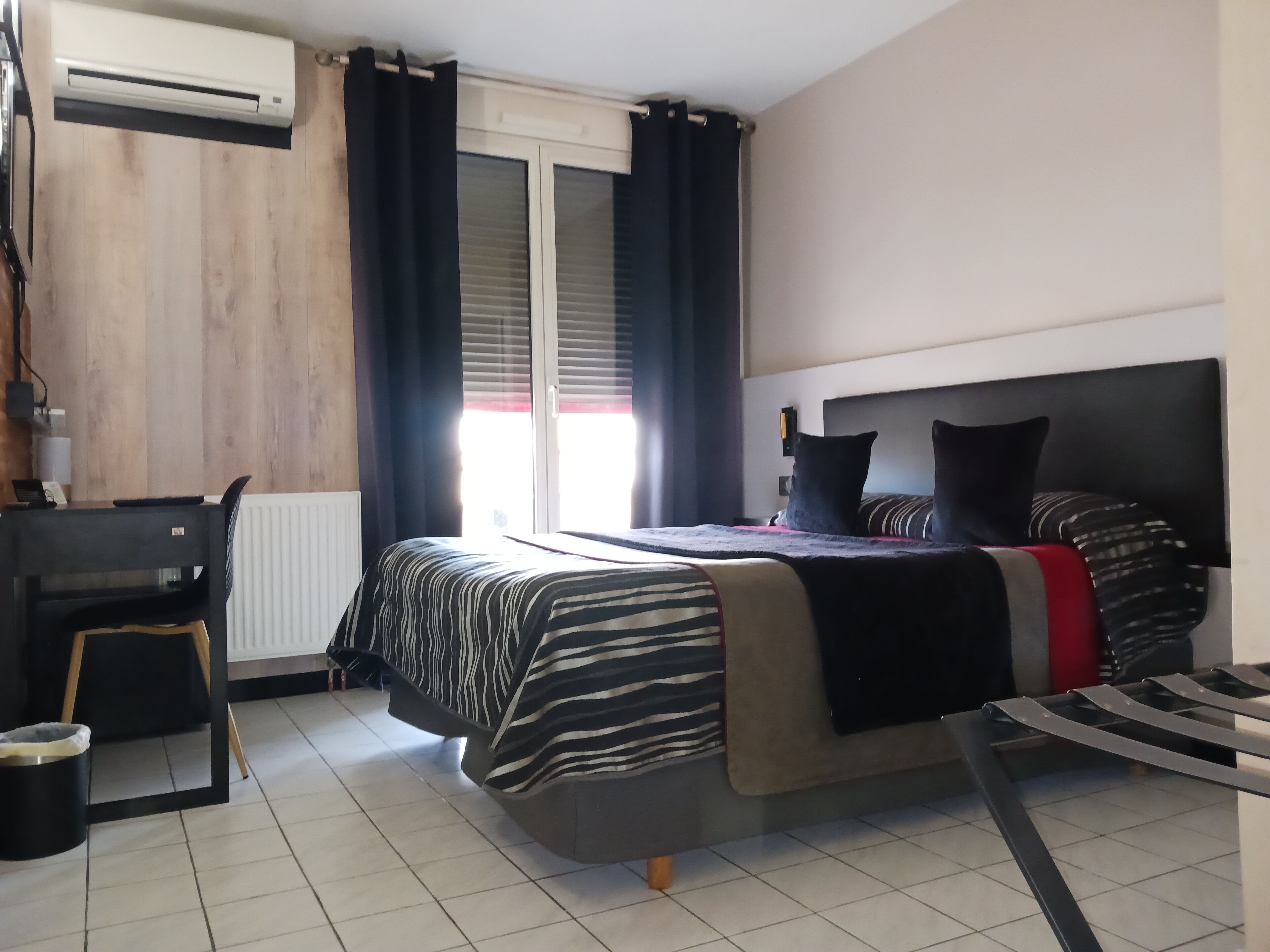 Hotellihuone, jossa on sänky, työpöytä ja ilmastointilaite.
