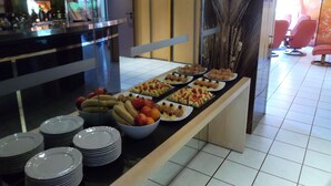 A buffet with various fruits and pastries, a bar area with bottles, and a seating area with chairs.