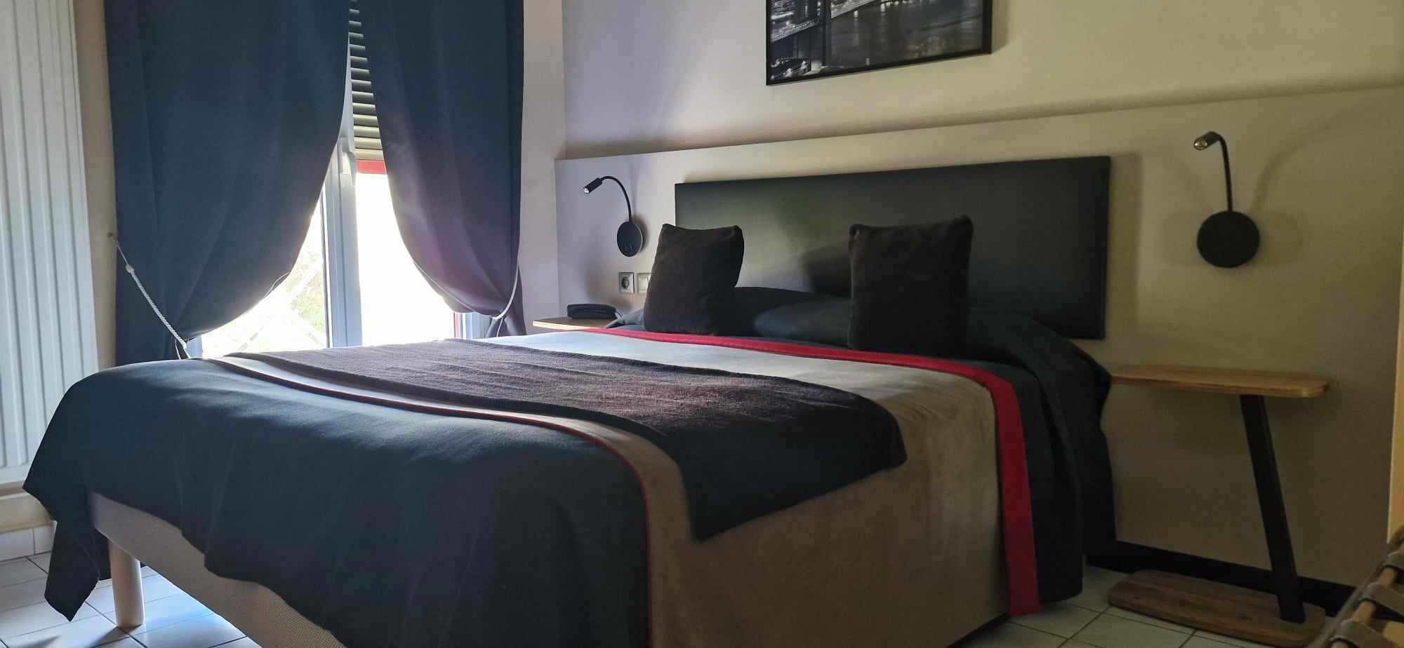 Ein ordentlich bezogenes Bett mit Kopfteil, ein Nachttisch mit Lampe und ein Fenster mit Vorhängen.