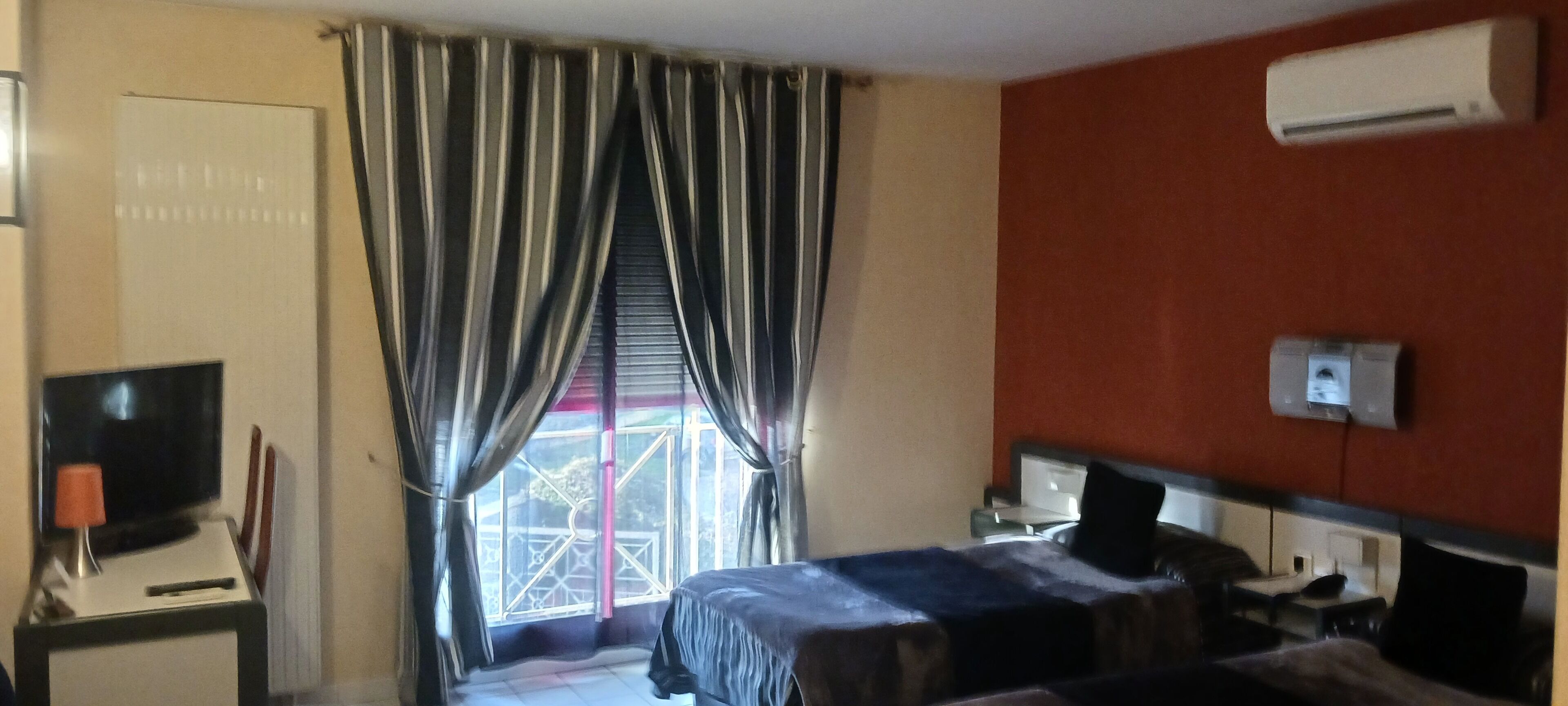 A hotel room with a bed, a TV, a desk, and a window with curtains.
