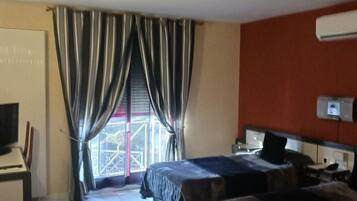 A hotel room with a bed, a TV, a desk, and a window with curtains.