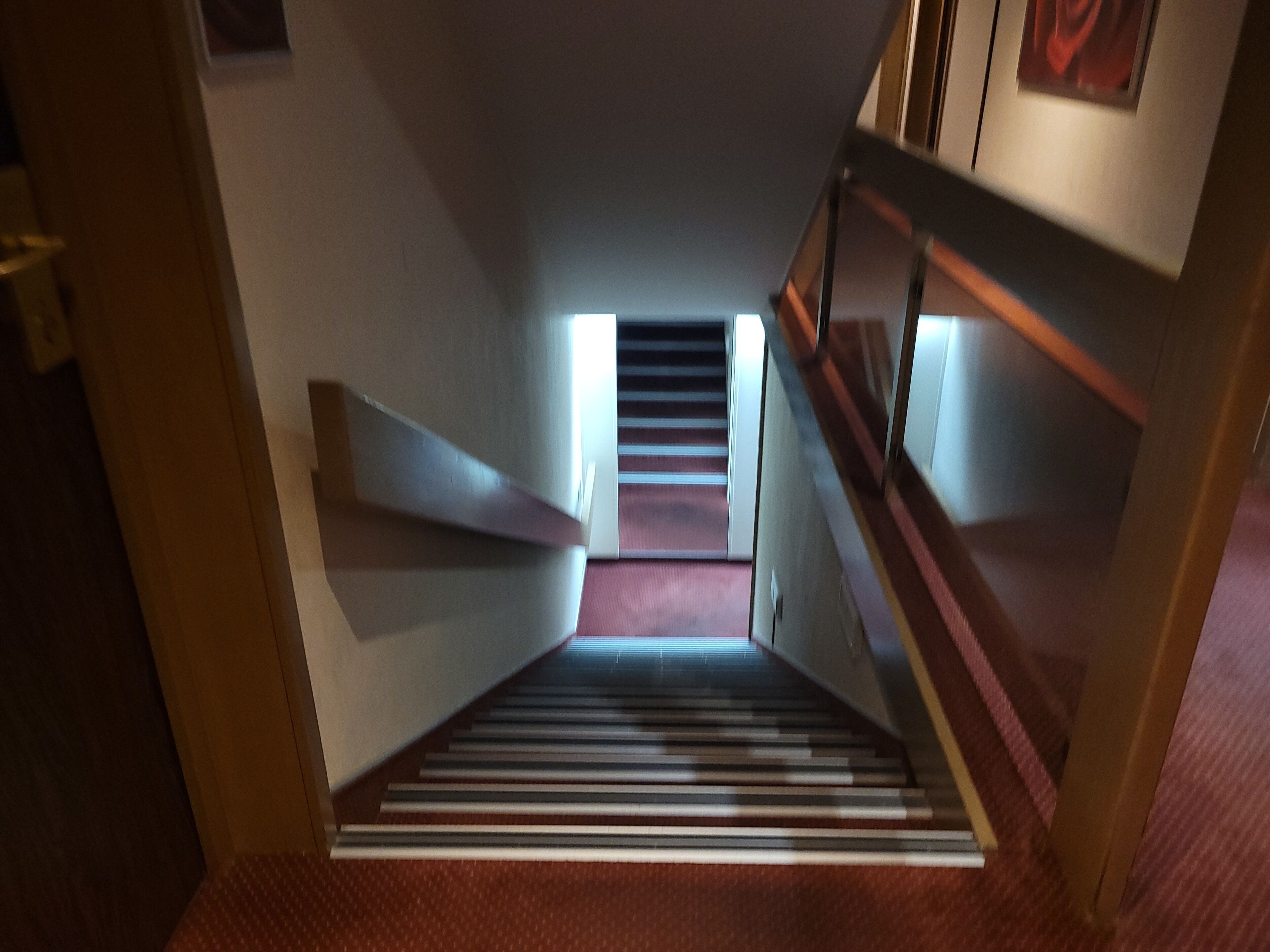 A staircase with a handrail, carpeted steps, and a landing area with a light fixture.