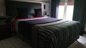 Quarto de hotel moderno com uma cama grande, televisão de tela plana e janela com persianas.