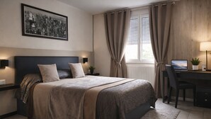 A bedroom with a large bed, a desk with a laptop, a potted plant, and a cityscape painting on the wall.