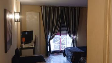 A hotel room with a bed, a desk with a TV, a window with curtains, and a door.
