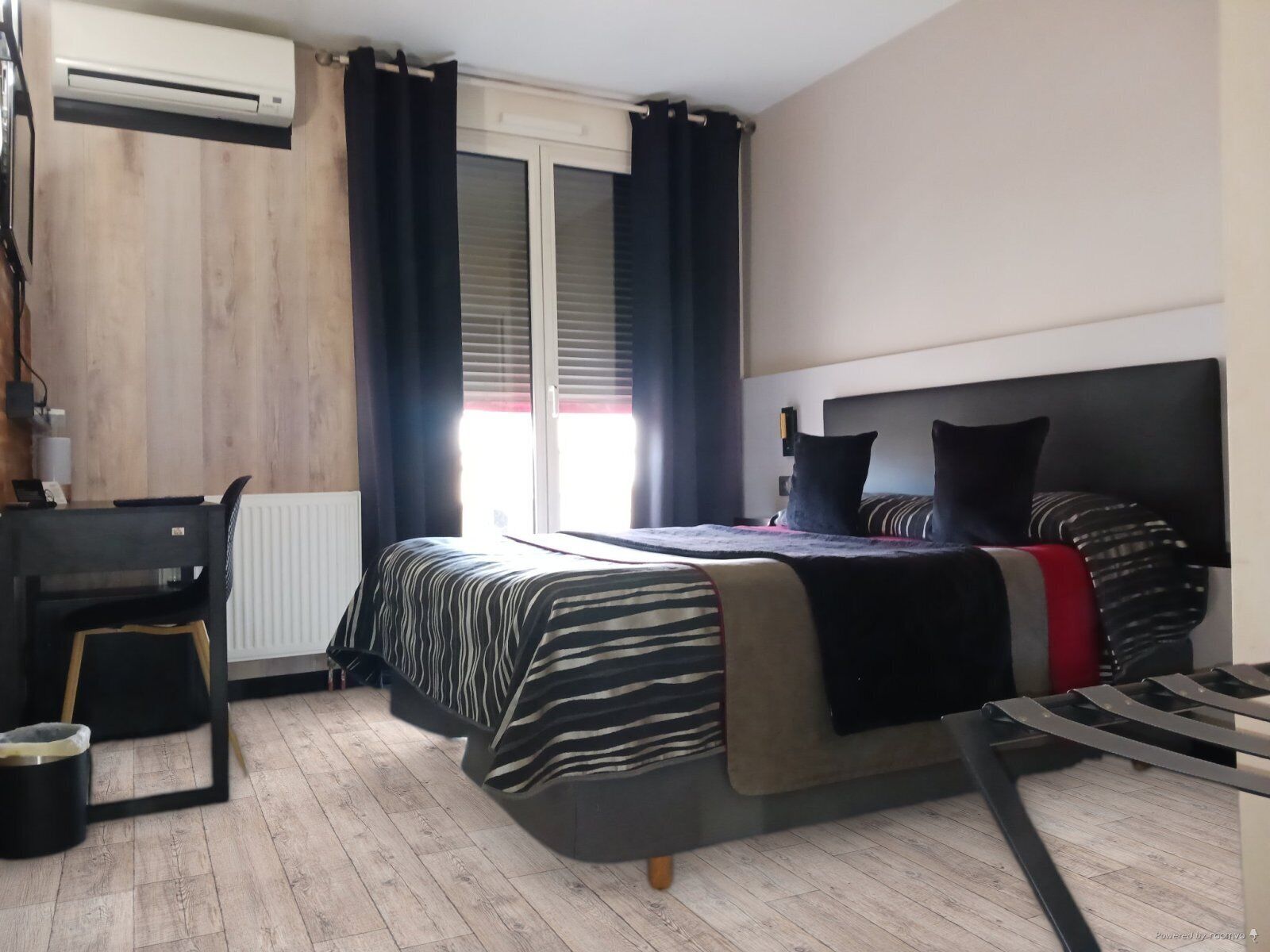 A bedroom with a bed, a desk, and an air conditioning unit.