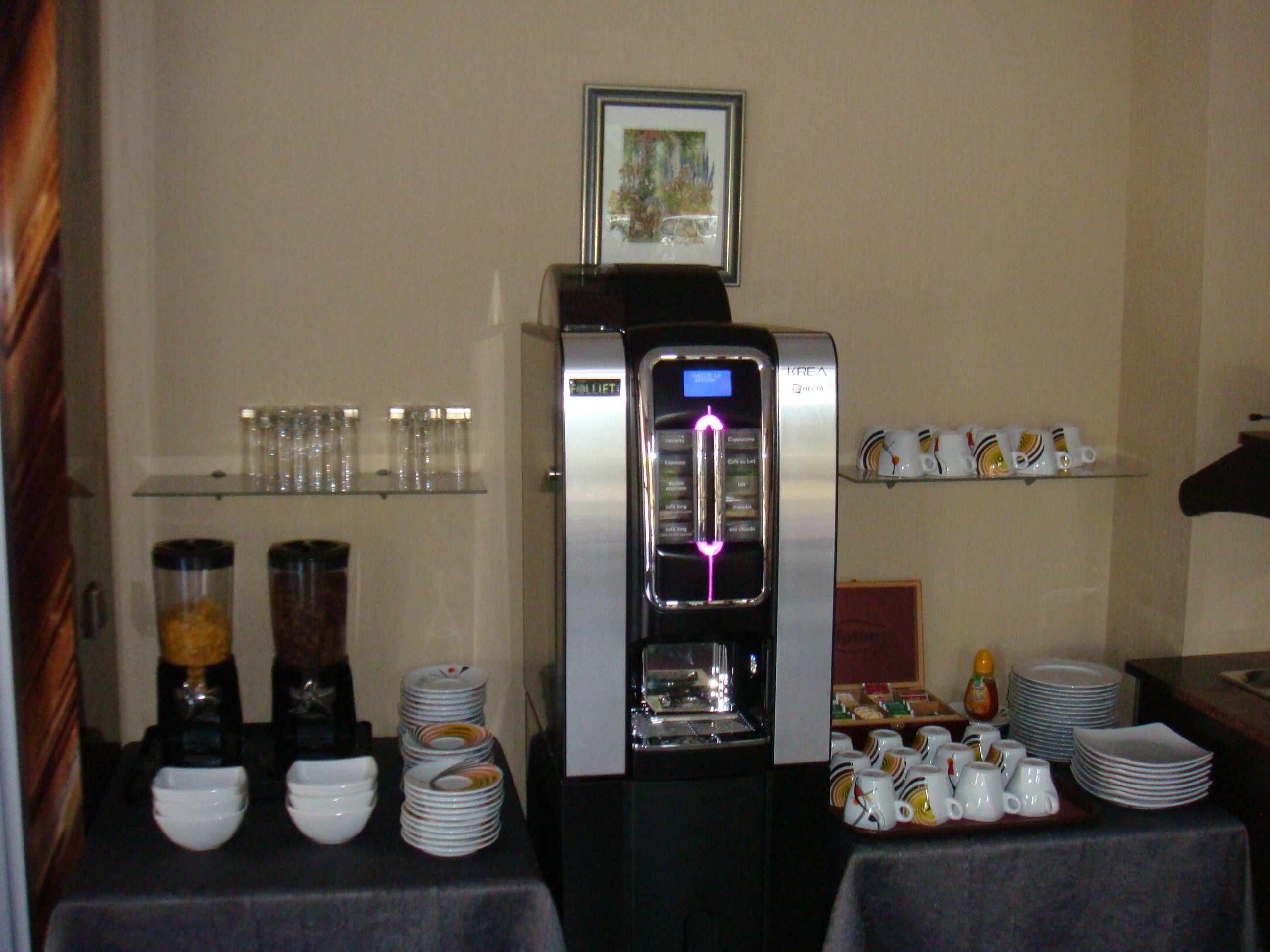Una estación de café autoservicio con cafetera, espumador de leche y diversas opciones de café.