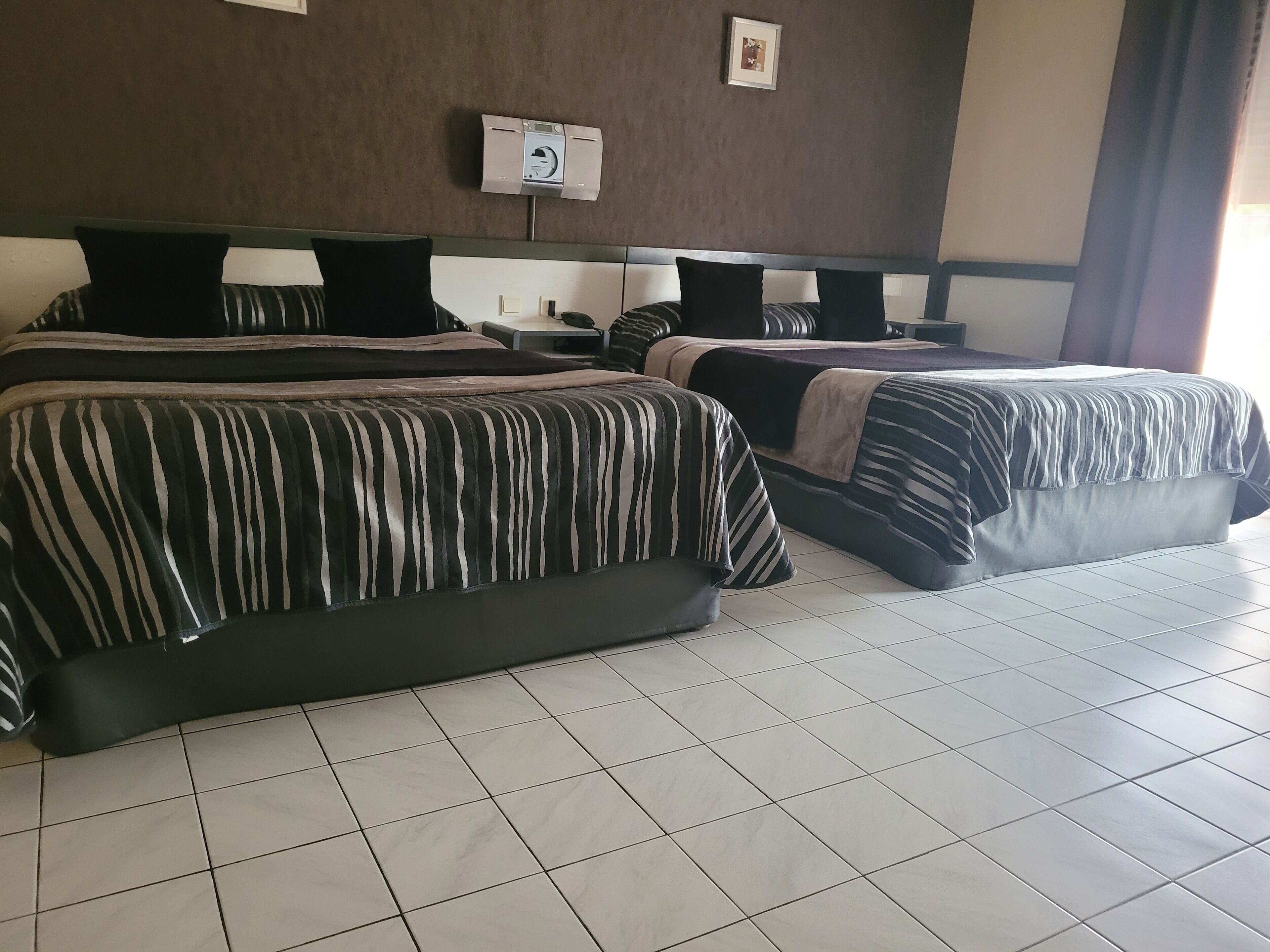 A hotel room with two beds, a wall-mounted air conditioning unit, and a tiled floor.