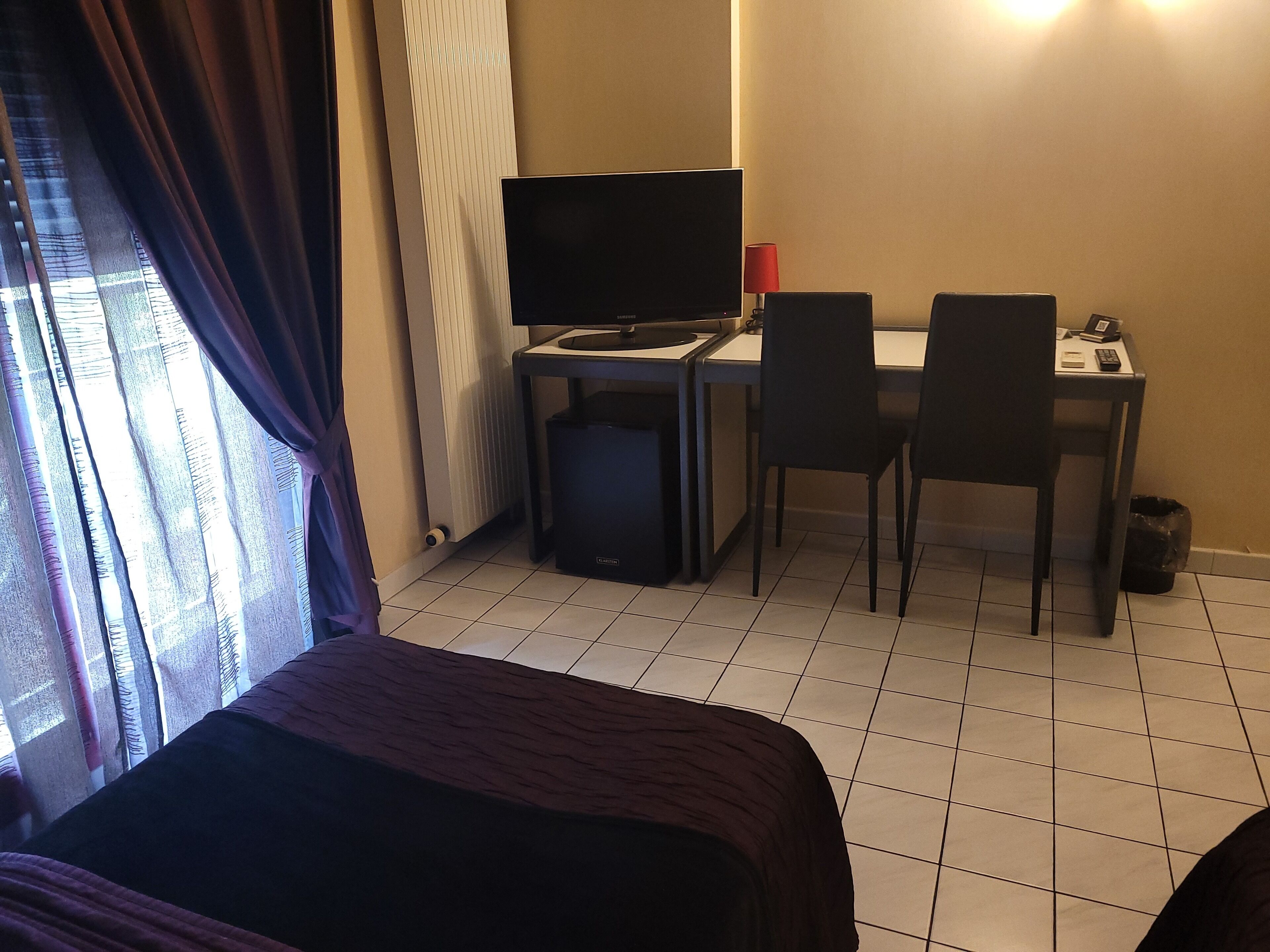 Een hotelkamer met een bed, een bureau met een computer en stoel, een televisie en een raam met gordijnen.