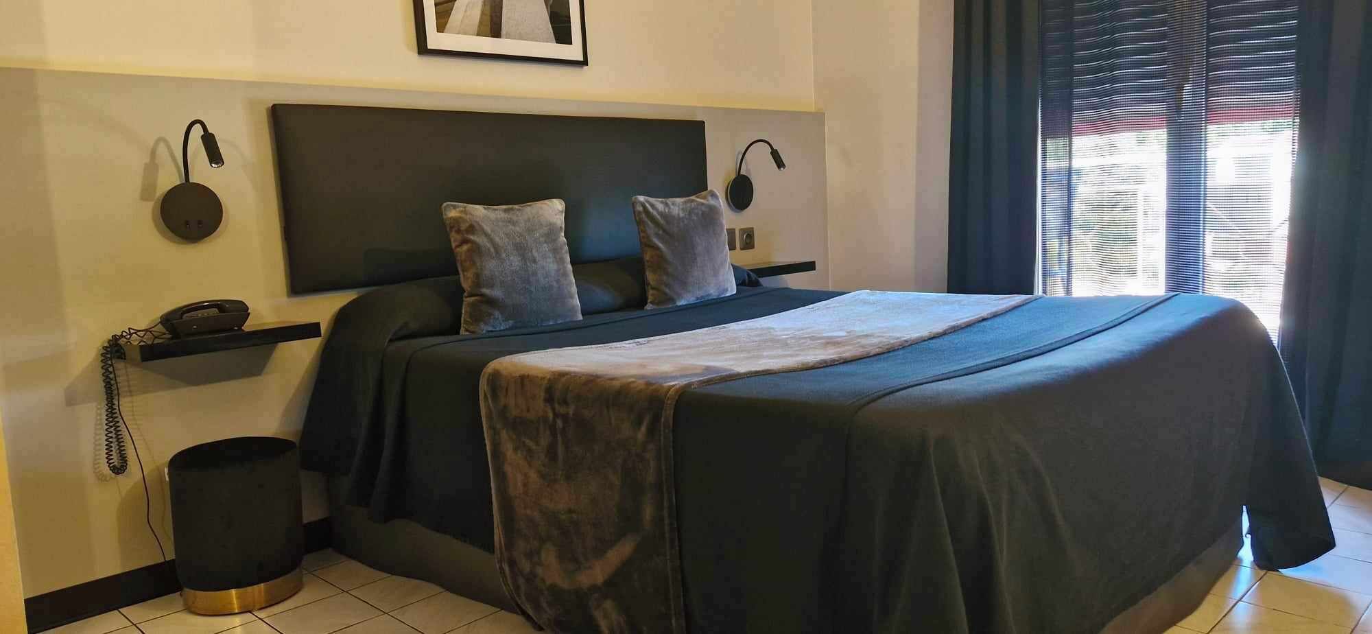 A hotel room with a bed, a bedside table, a lamp, and a telephone.