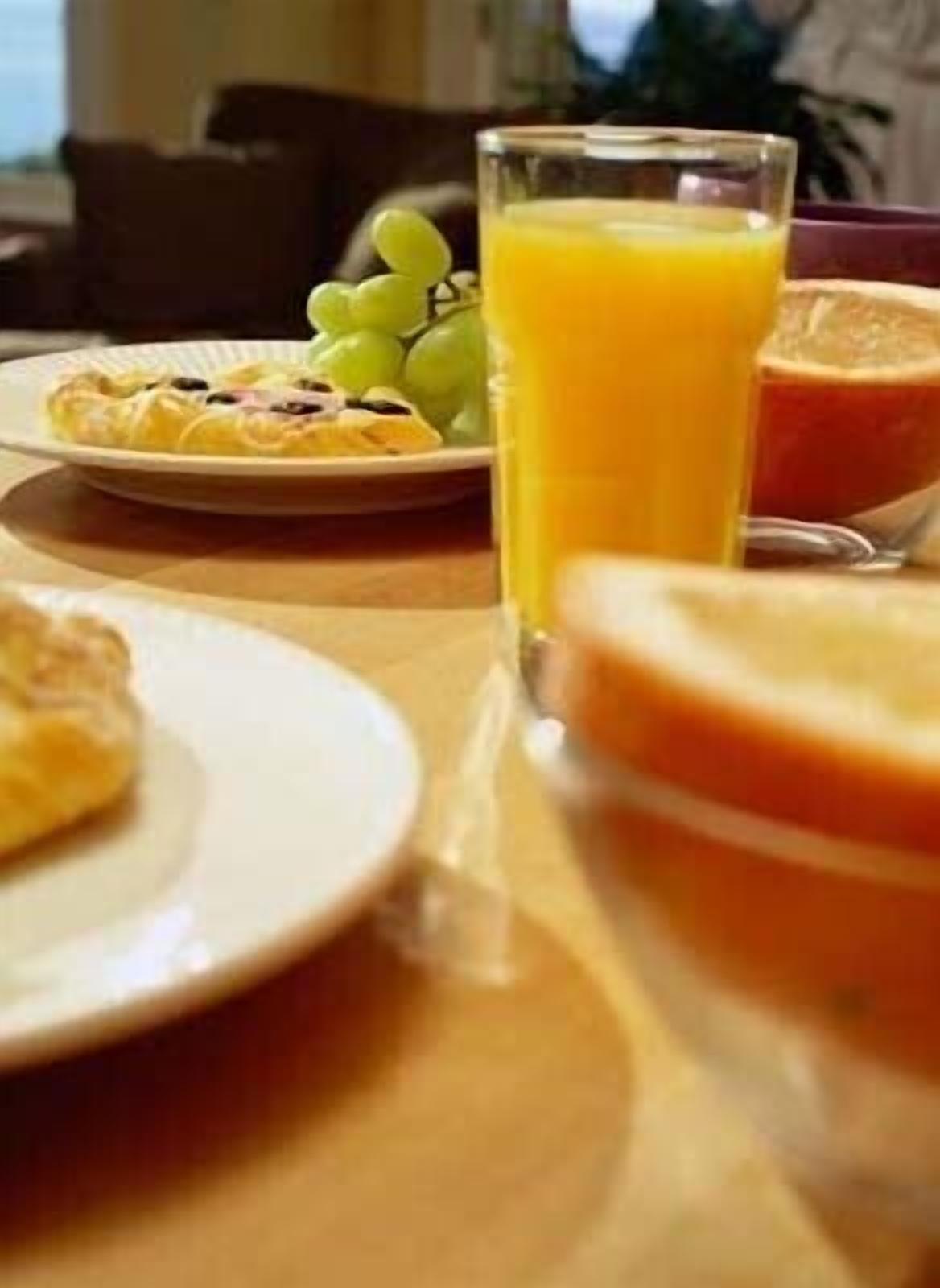 Una mesa de desayuno con un plato de comida, un vaso de jugo de naranja y un tazón de fruta.