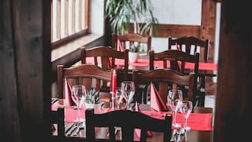 A dining area with wooden tables and chairs, red tablecloths, and potted plants.