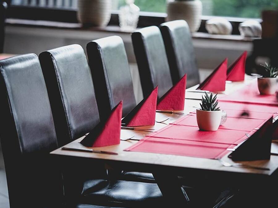 Un ambiente de restaurante con sillas de cuero y servilletas rojas sobre una mesa de madera.