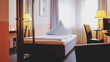 A hotel room with a bed, a desk, a chair, and a window with curtains.
