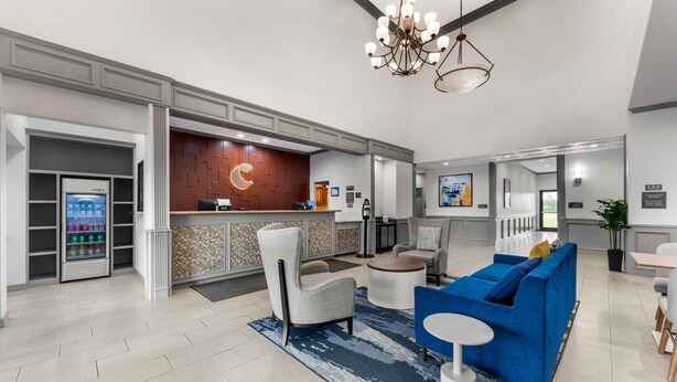 Een moderne hotellobby met een receptiebalie, een zithoek en een automaat.