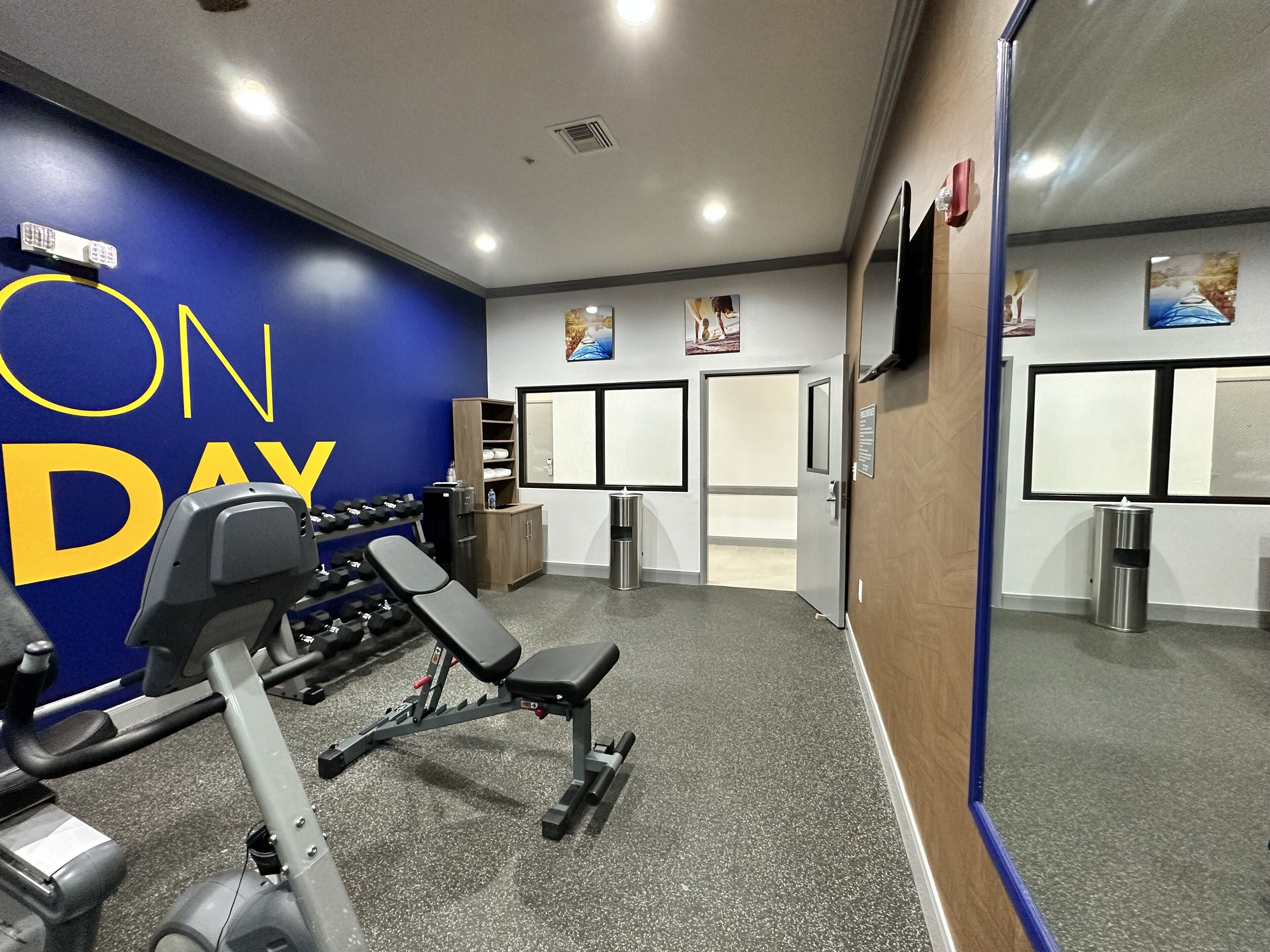 A gym with exercise equipment, a blue wall with 'ON DAY' text, a mirror, and a door with a window.