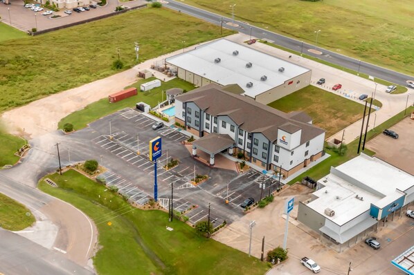 An aerial view of a commercial building with a parking lot, a gas station, and a swimming pool.