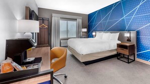 Een hotelkamer met een bed, nachtkastje, bureau, stoel en een groot raam.