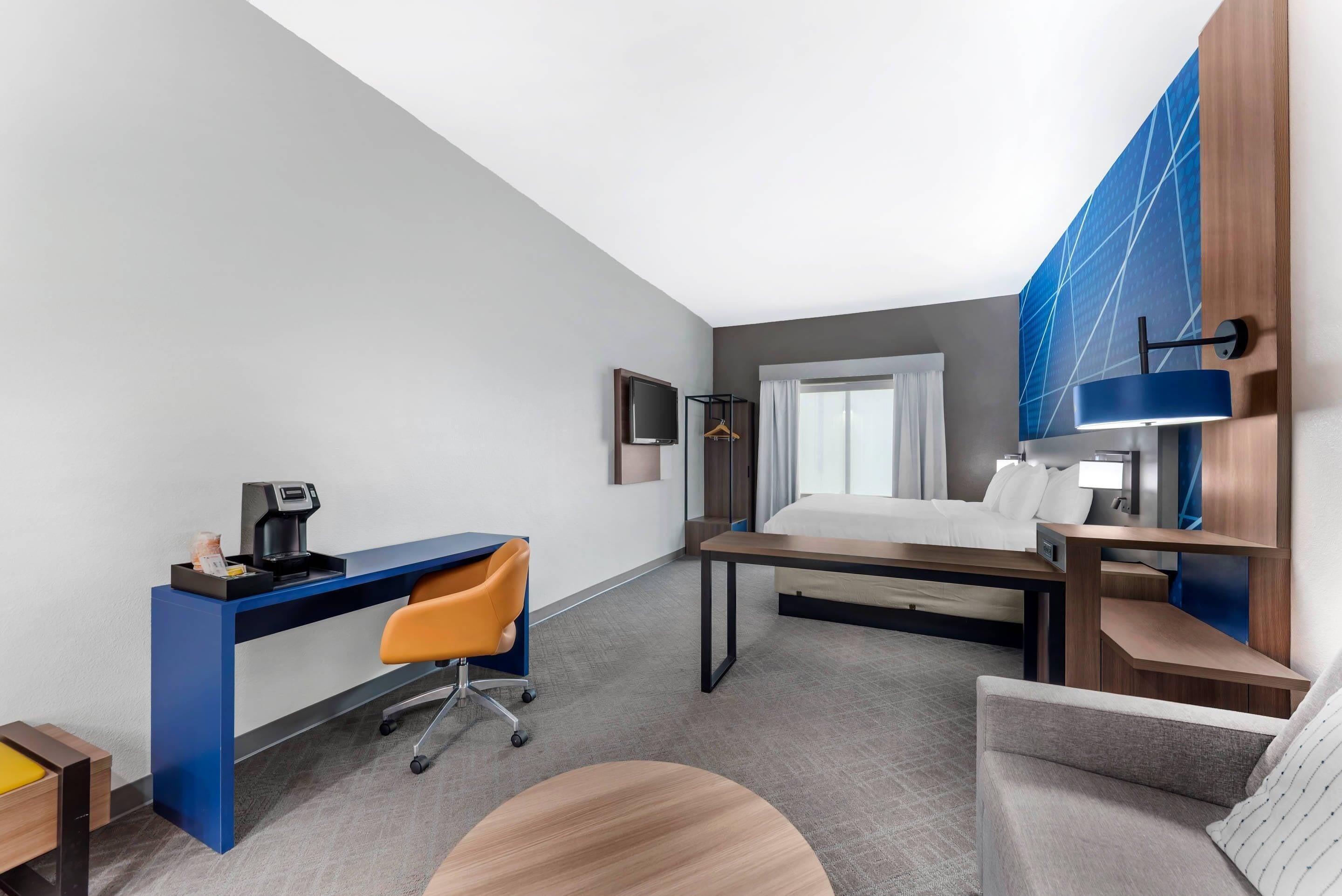 A modern hotel room with a desk, a bed, a sofa, and a TV.