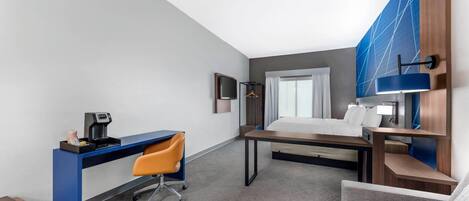 A modern hotel room with a desk, a bed, a sofa, and a TV.